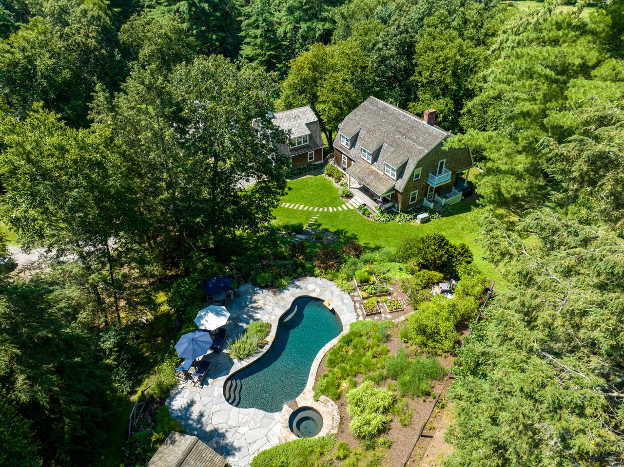 Aerial view of a charming house with a swimming pool surrounded by lush greenery in a serene setting.